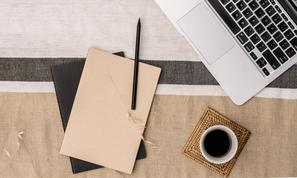 journaling setup with notebooks, pen, laptop, and coffee on a neutral surface
