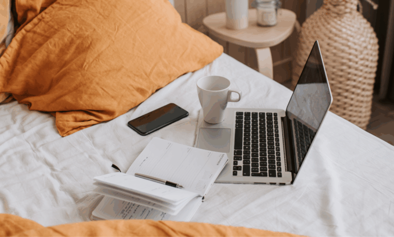 writing and journaling from bed with laptop, notebook, and coffee