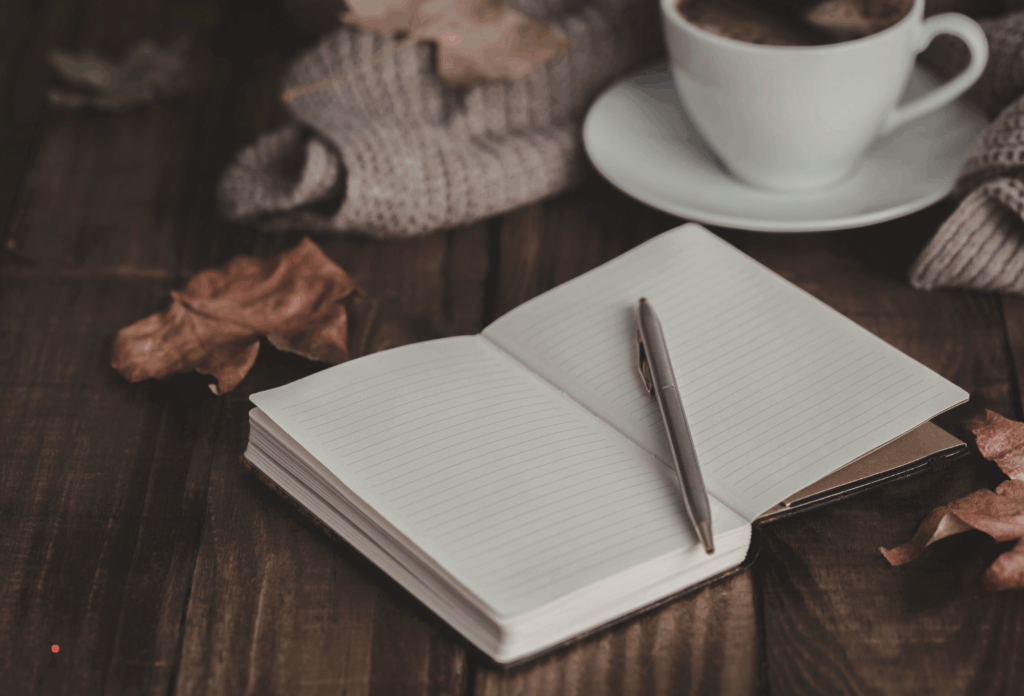 open notebook and pen beside a cup of coffee in a reflective setting
