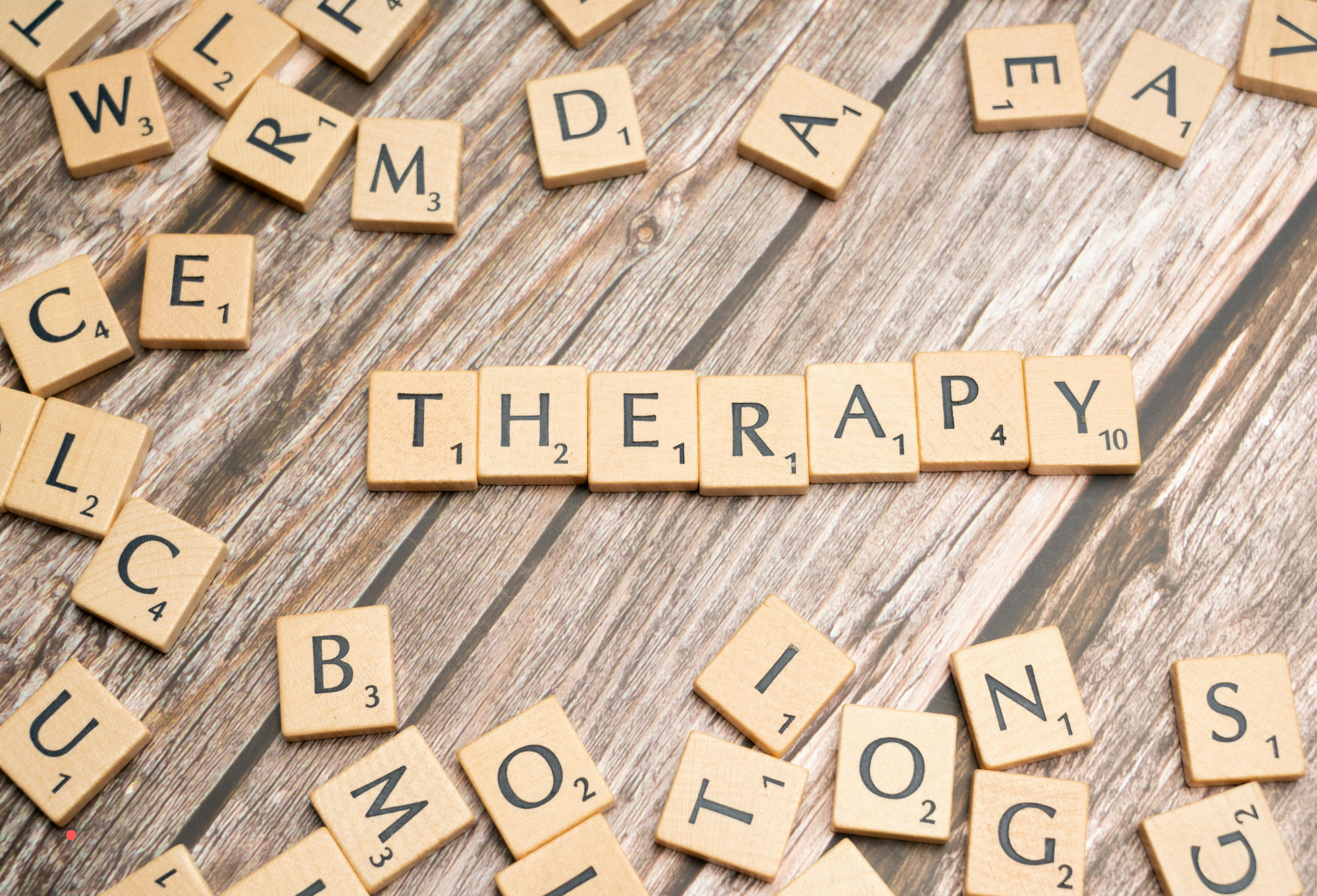 Wooden letter tiles spelling “THERAPY” scattered on a table, symbolizing therapeutic writing and self-reflection