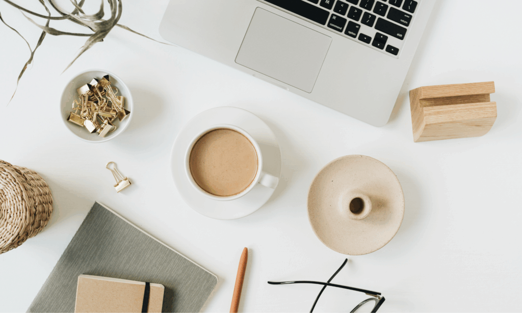 minimal writing workspace with coffee, notebook, and laptop on a white desk