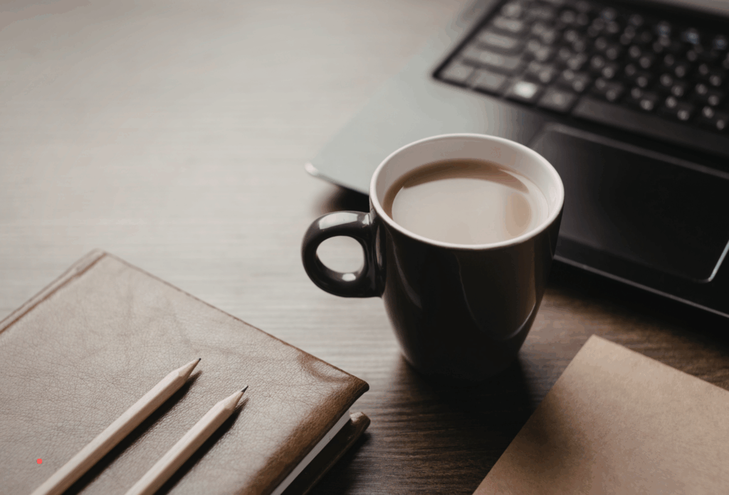writing setup with notebook, pencils, and coffee beside a laptop