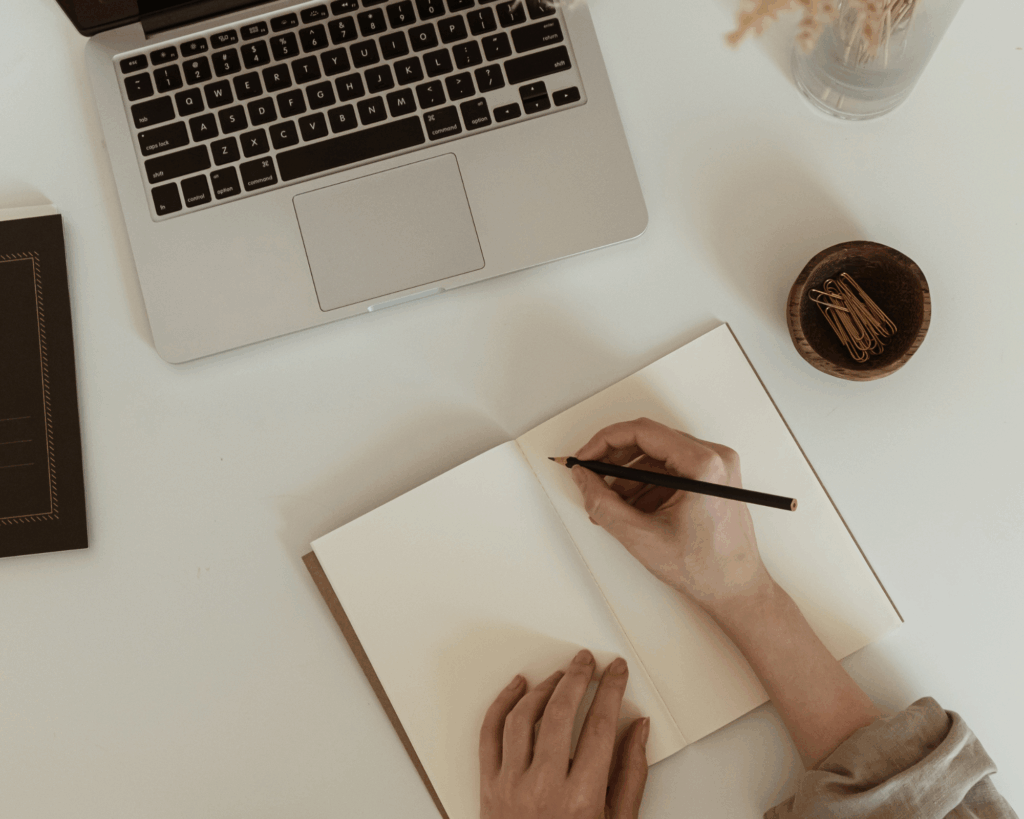 Person writing in a notebook next to a laptop, mindful writing practice