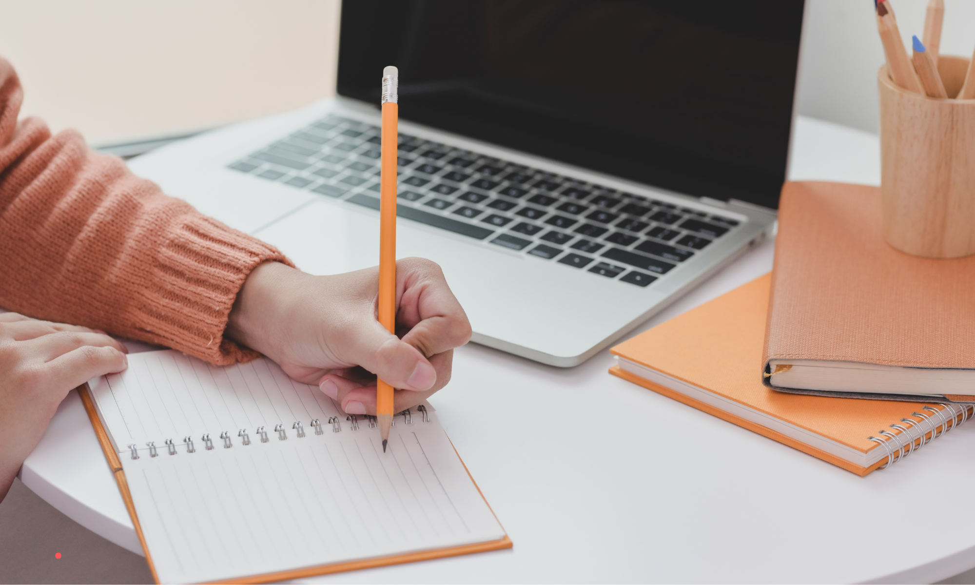 Person writing in a notebook beside a laptop, representing a reflective journaling practice.