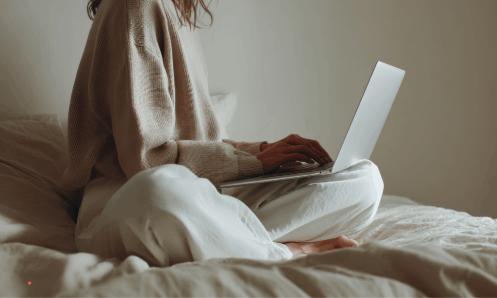 Person sitting on a bed while writing on a laptop, representing a gentle and personal journaling practice at home