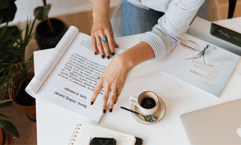 Person reviewing handwritten notes and journaling prompts at a desk with a cup of coffee.